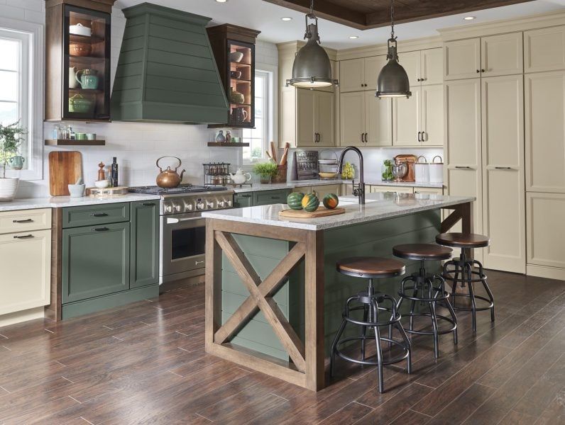 Spacious kitchen with green and cream cabinets, wooden island, pendant lights, and stainless steel appliances.