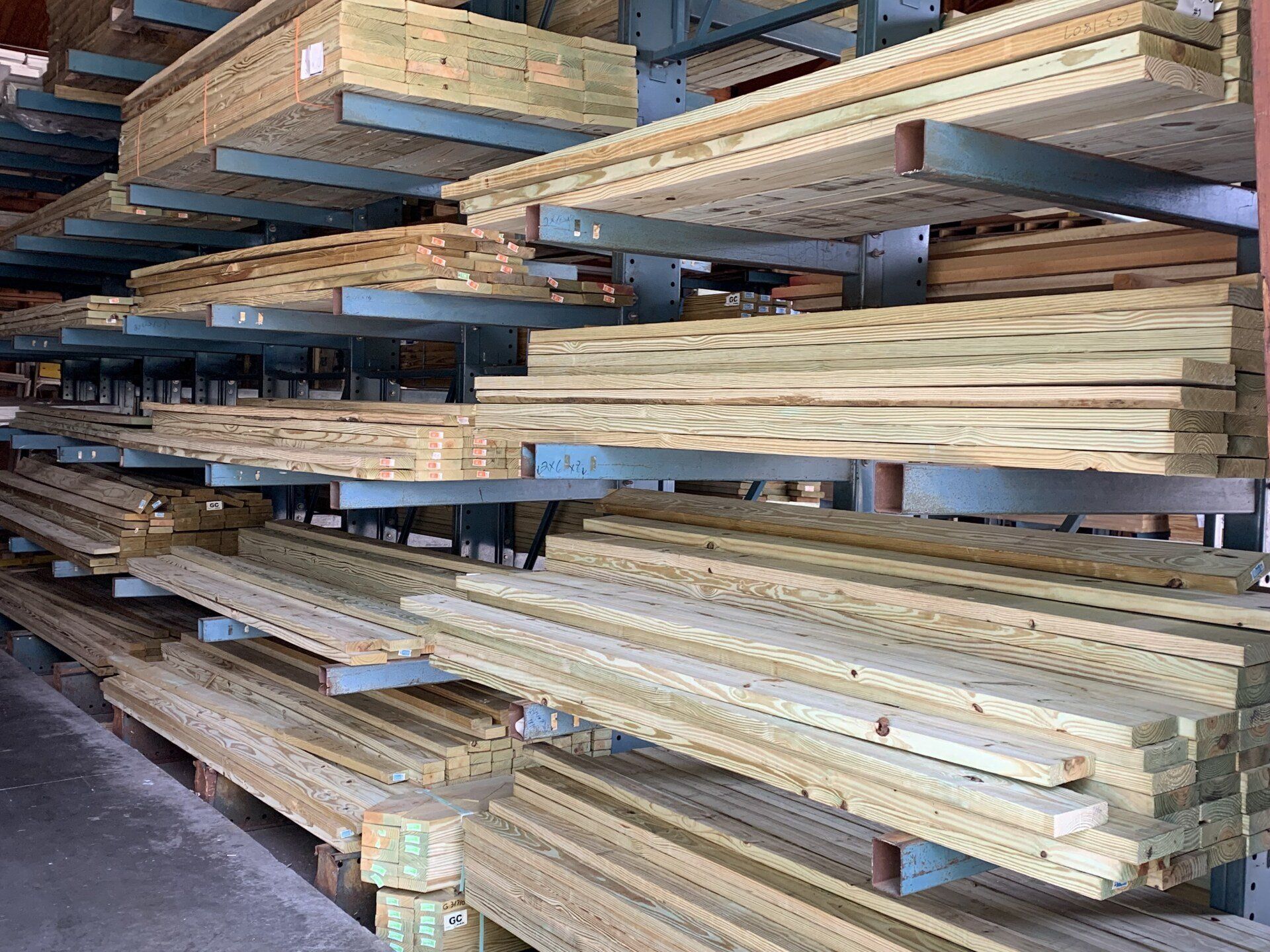 Lumberyard with shelves of stacked wooden planks, varying sizes. Light wood tones, metal supports.