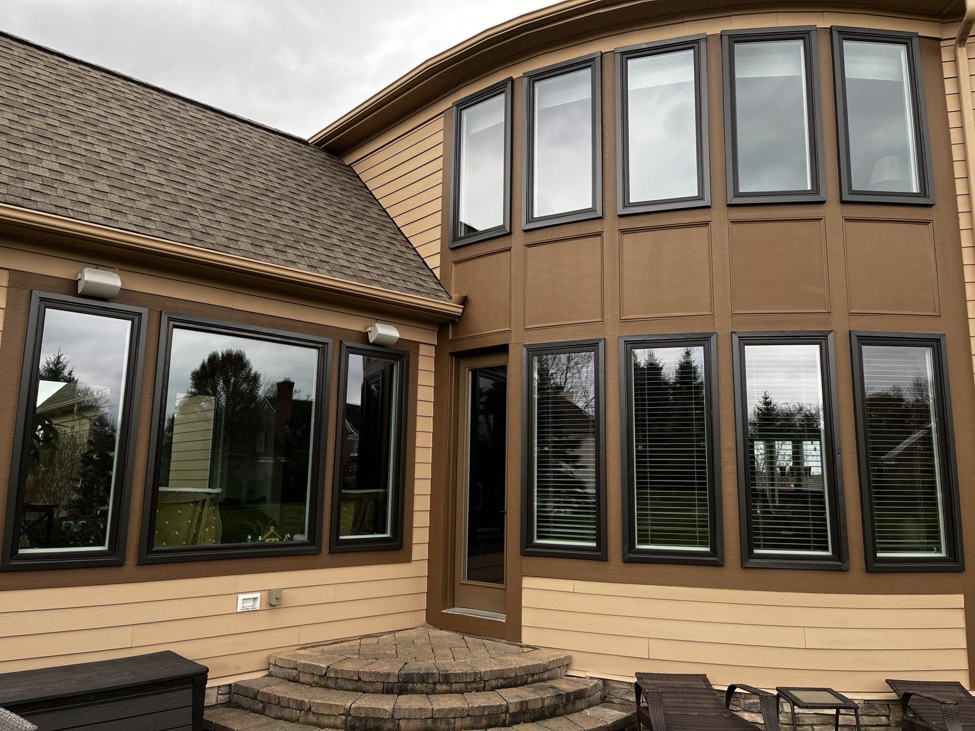 Brown house exterior with large windows reflecting the cloudy sky.