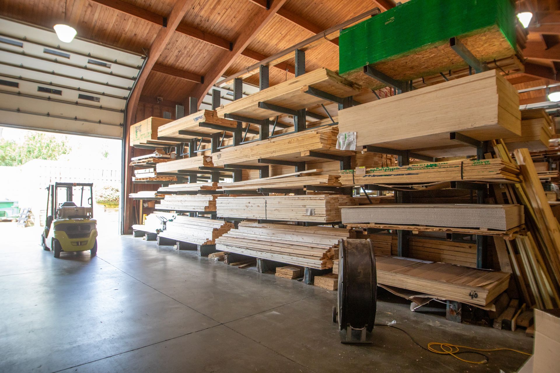 Inside a lumberyard; stacks of wood on shelving, forklift in the open doorway.