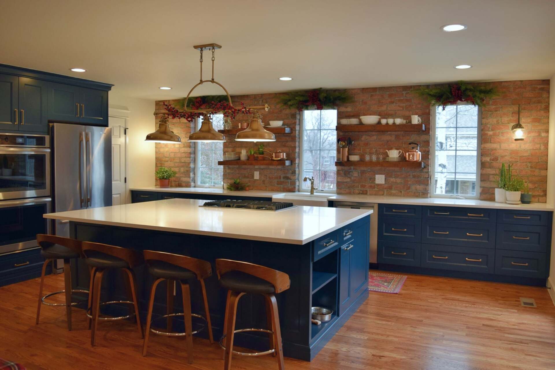 Spacious kitchen with blue cabinets, white countertops, brick wall, and a large island with bar stools.