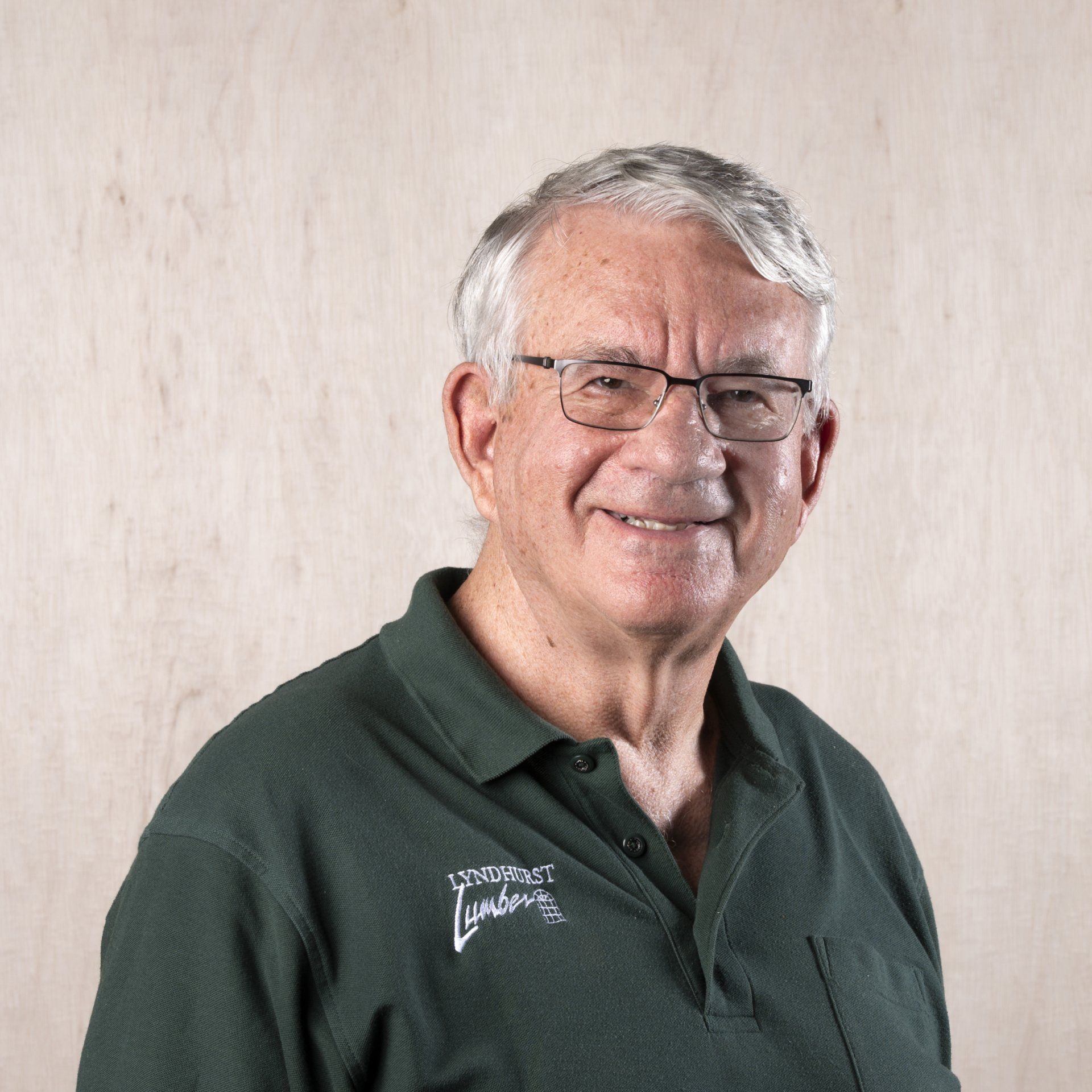 Man with gray hair and glasses wearing a green polo shirt smiling.