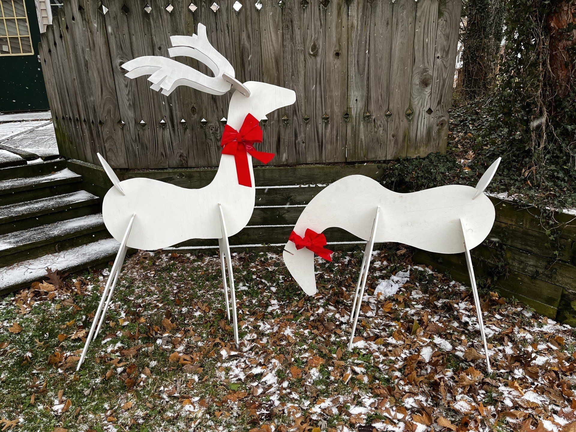 Two white reindeer yard decorations with red scarves, on snowy ground.
