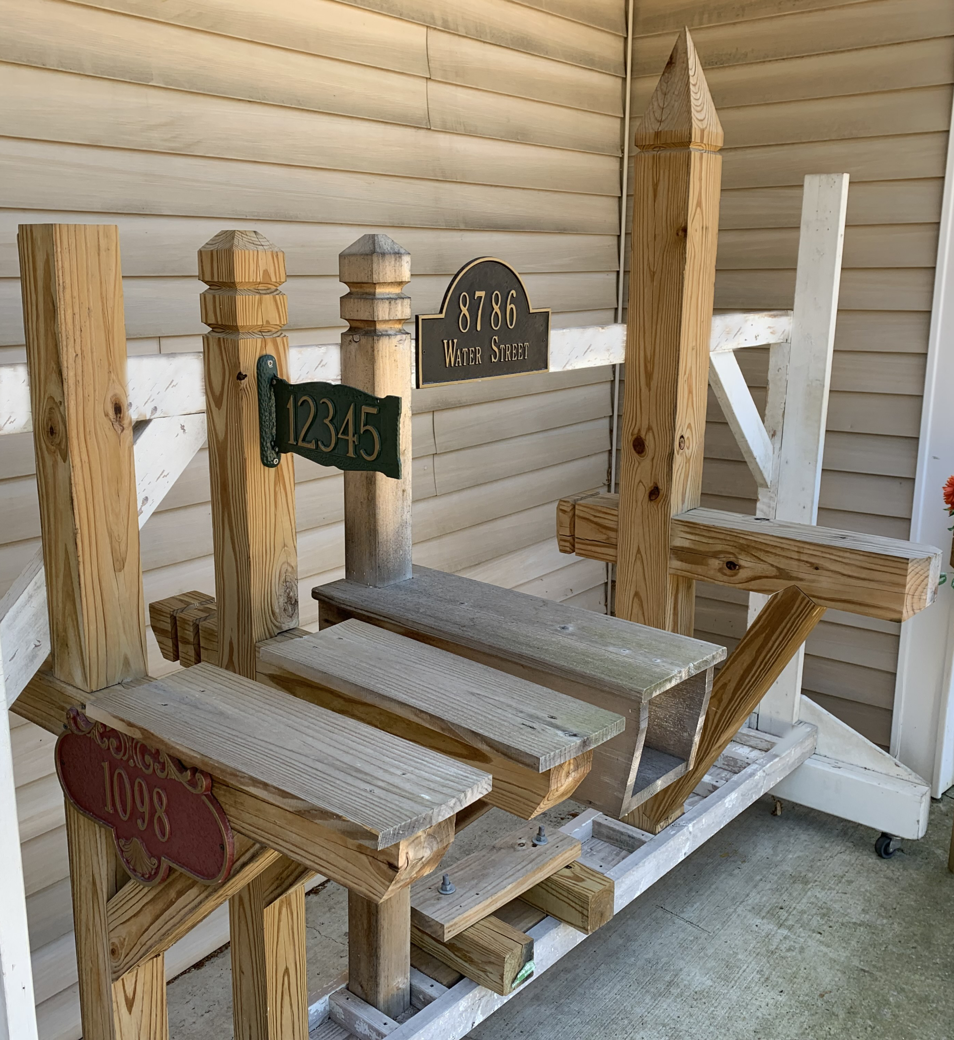 Wooden mail center with multiple platforms, address sign, and decorative elements against a house wall.