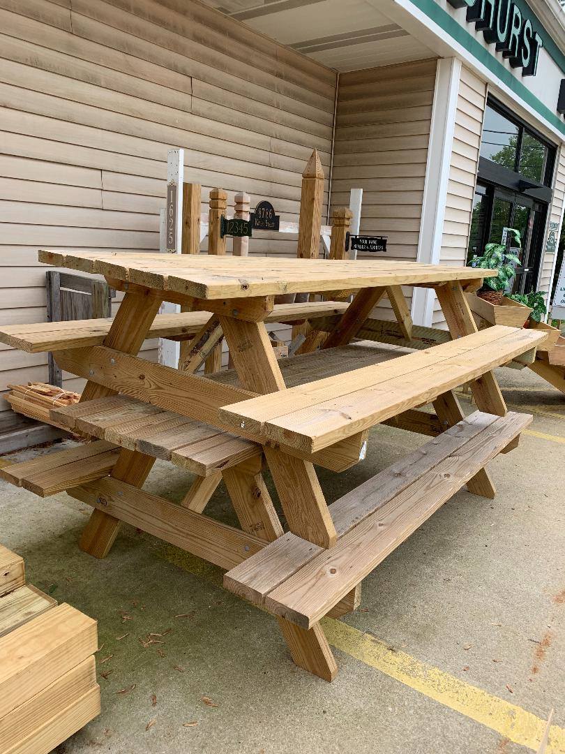 Wooden picnic tables stacked outside a building with horizontal siding.