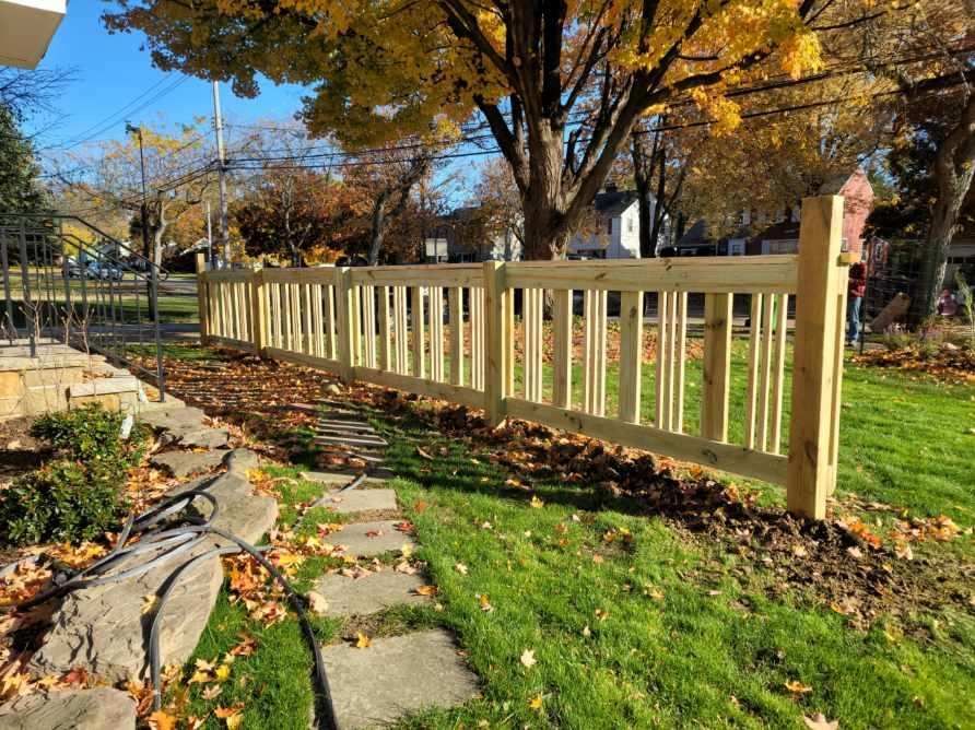 Wooden fence along a grassy yard with stepping stones and autumn leaves.