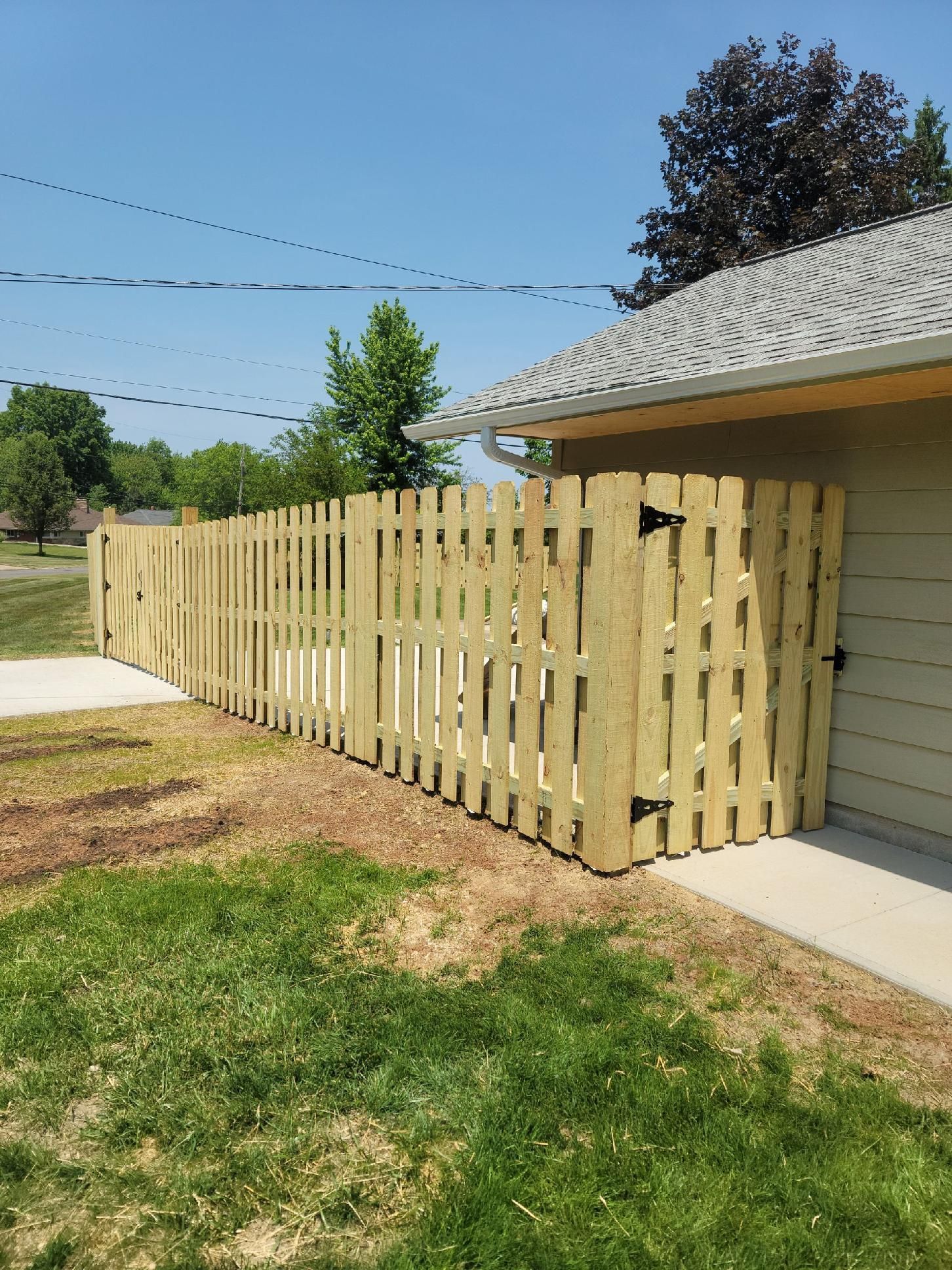 Wooden picket fence beside a building, on a sunny day. Green grass and blue sky.