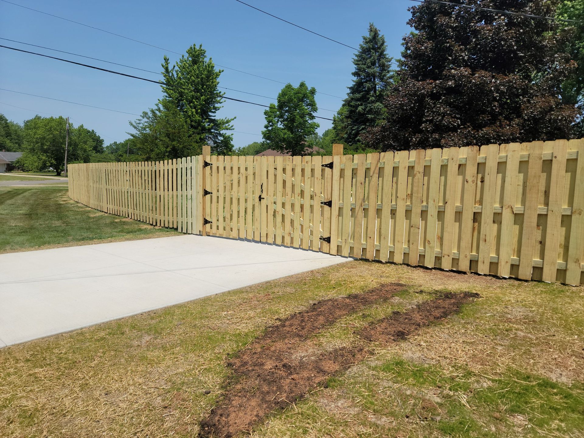 Wooden fence with gate next to a concrete driveway and grassy yard on a sunny day.