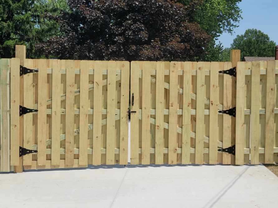 Wooden double gate with black hinges and latch, set in a concrete driveway.