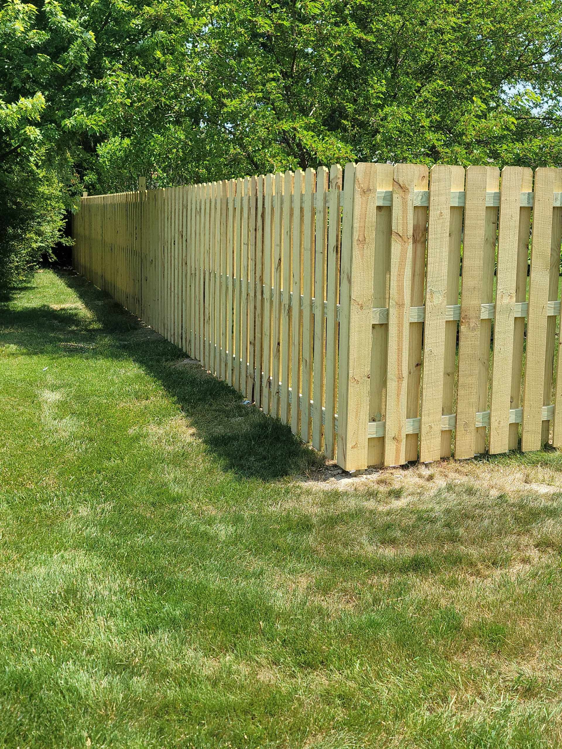 Wooden fence along a grassy lawn, with green trees in the background.