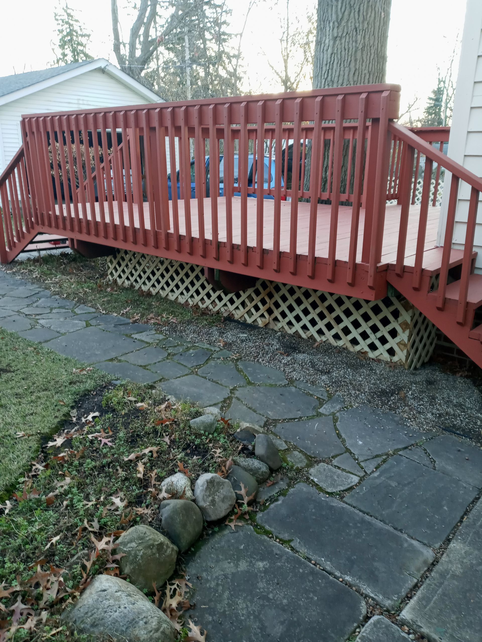 Red-painted wooden deck with railing, lattice skirting, and stone pathway.