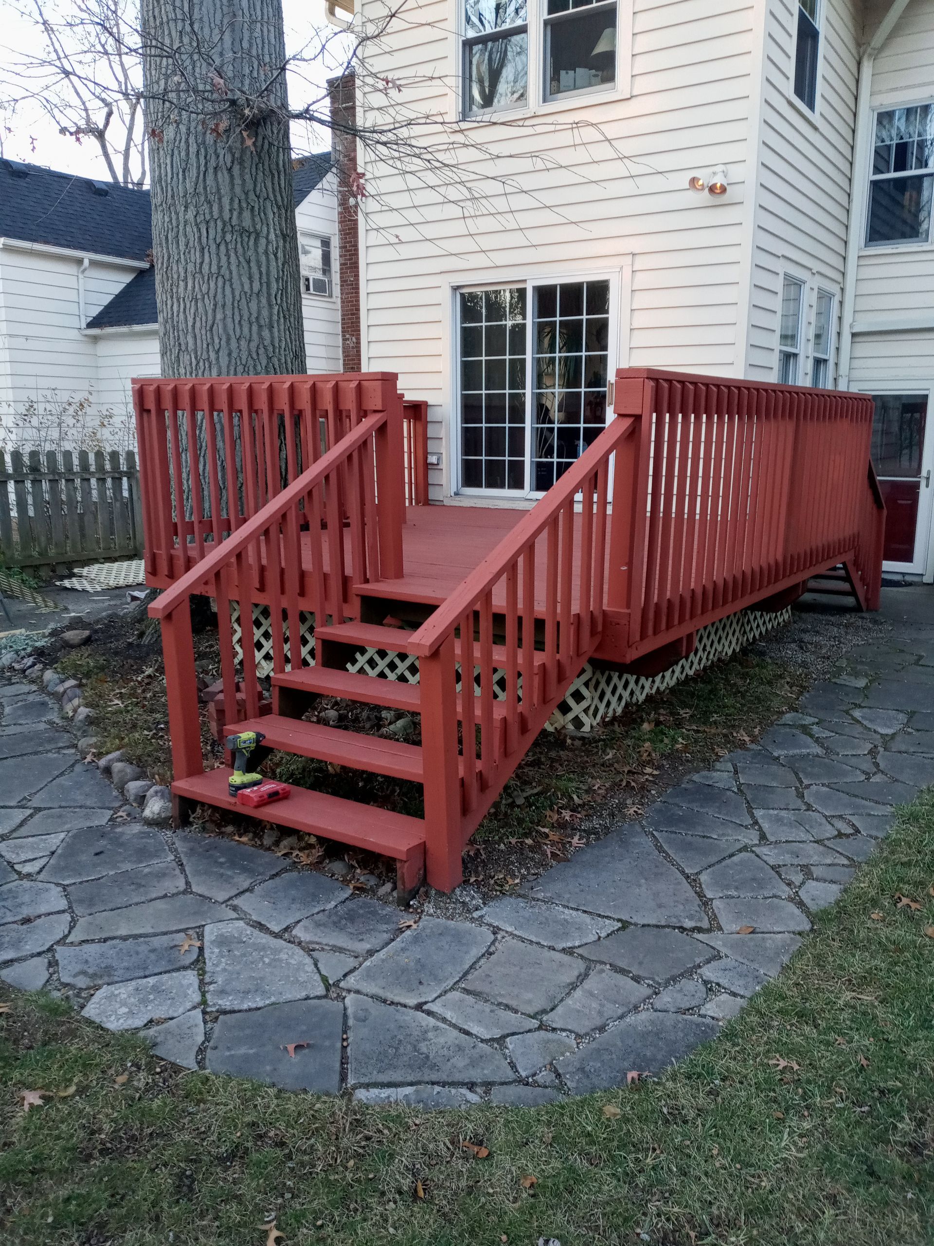 Red wooden deck with stairs and railing outside a light-colored house.