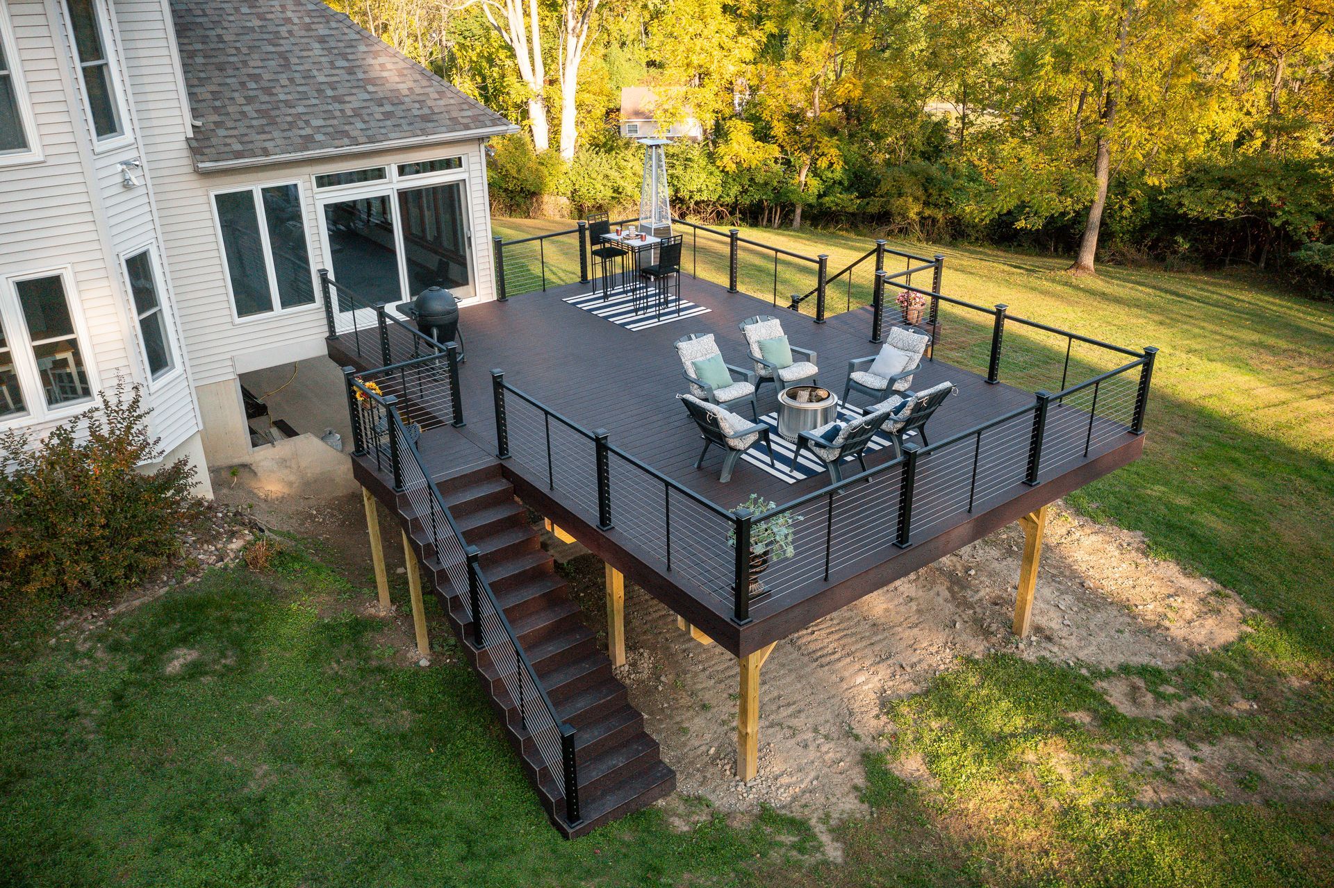 Elevated wooden deck with black railings and stairs, furnished with seating and a grill, attached to a house.