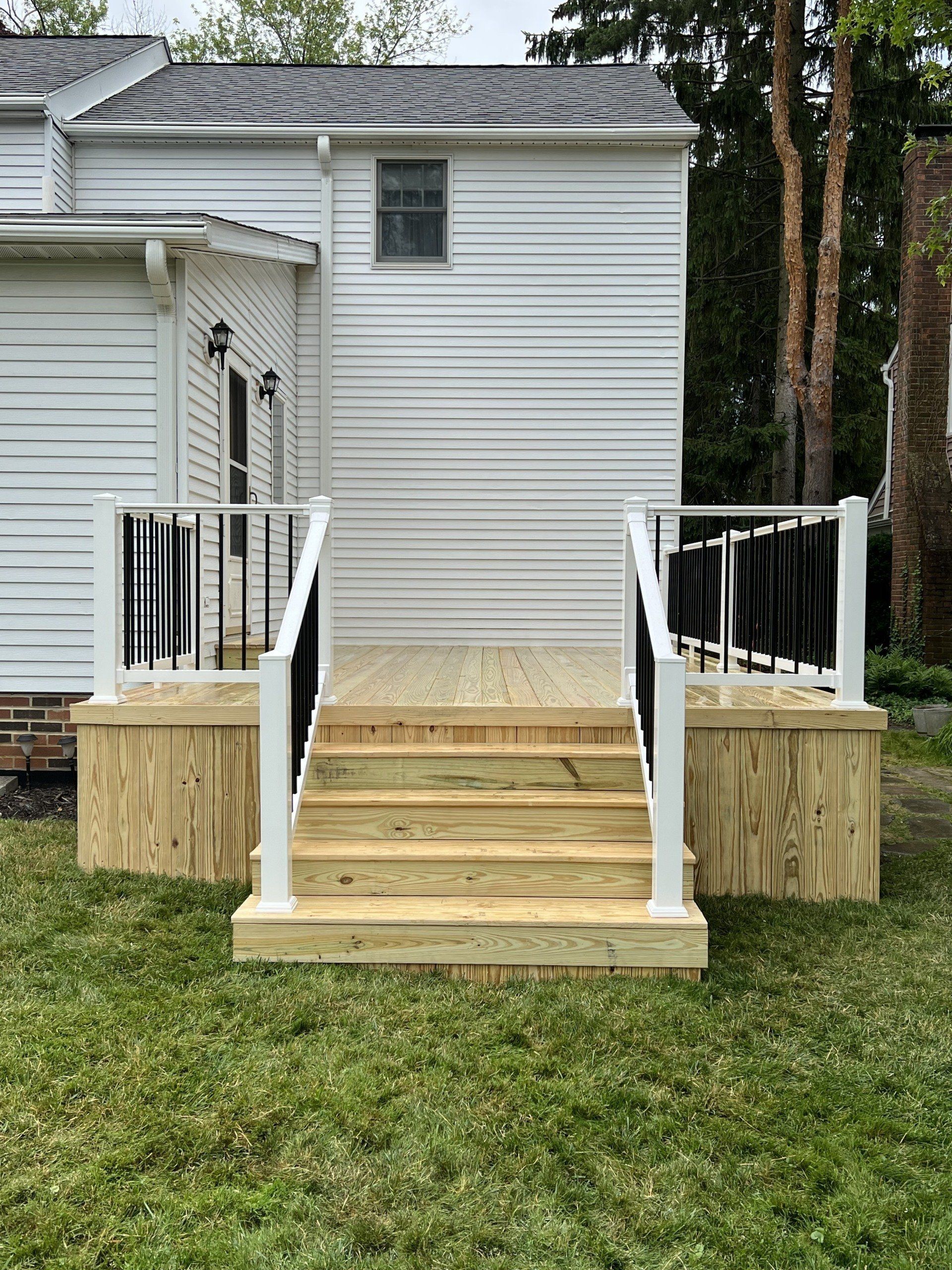 Wooden deck with stairs leading to a white building. Black railings on each side with grass in the foreground.