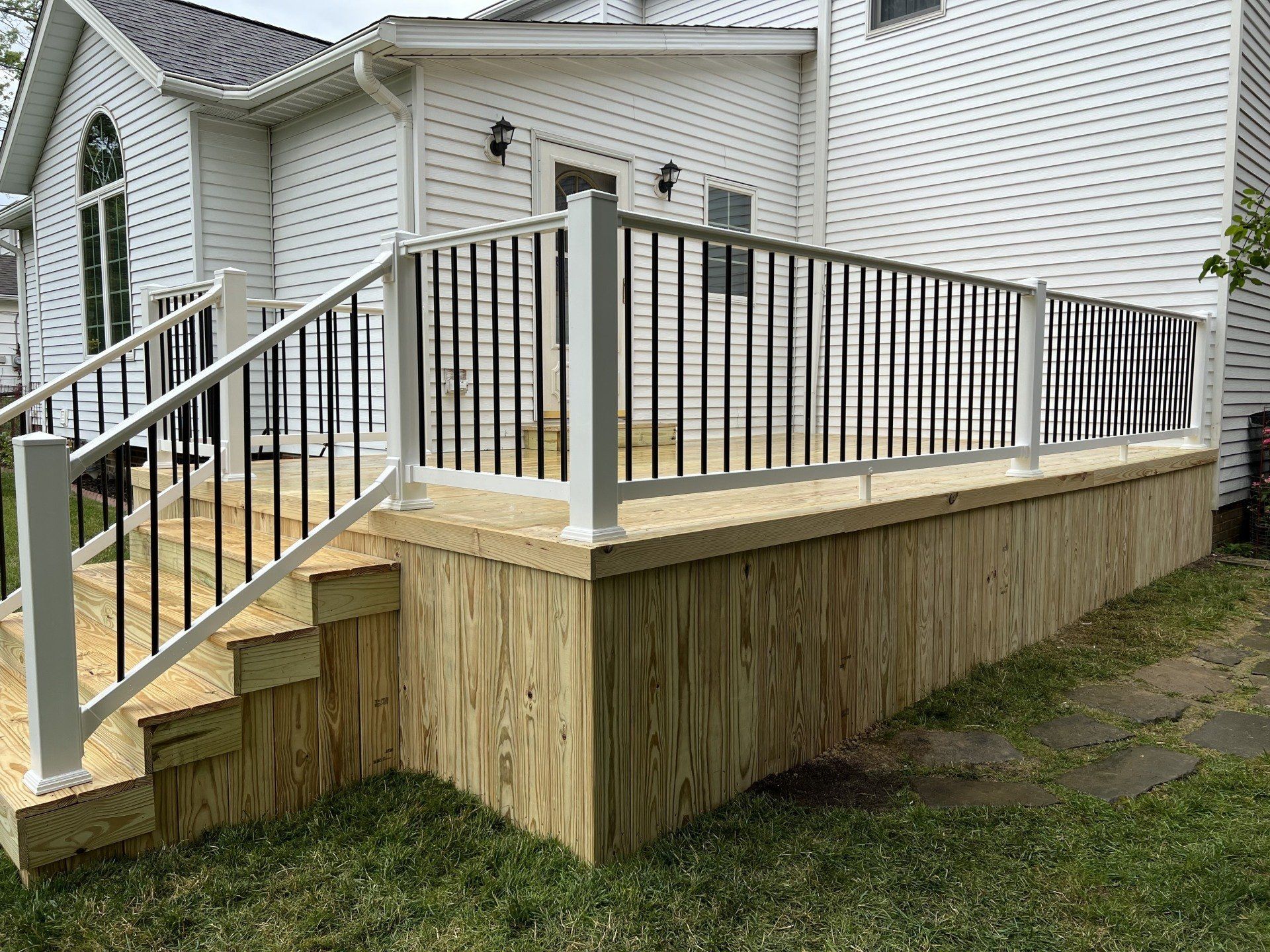 Wooden deck with white railings, black vertical bars, and steps leading to a house with white siding.