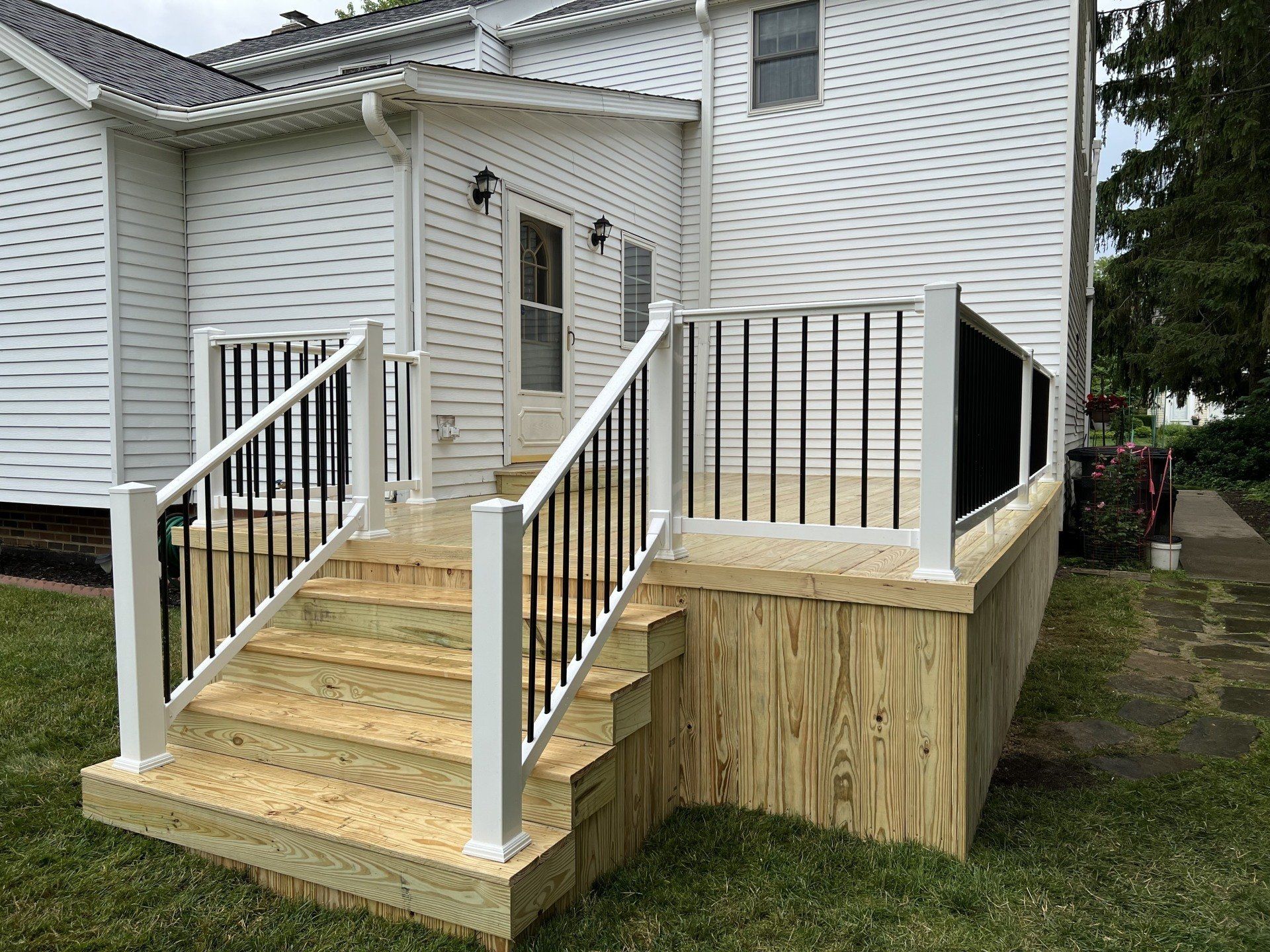Exterior view of a raised wooden deck with white railing, black vertical spindles, and stairs leading down to a grassy yard.