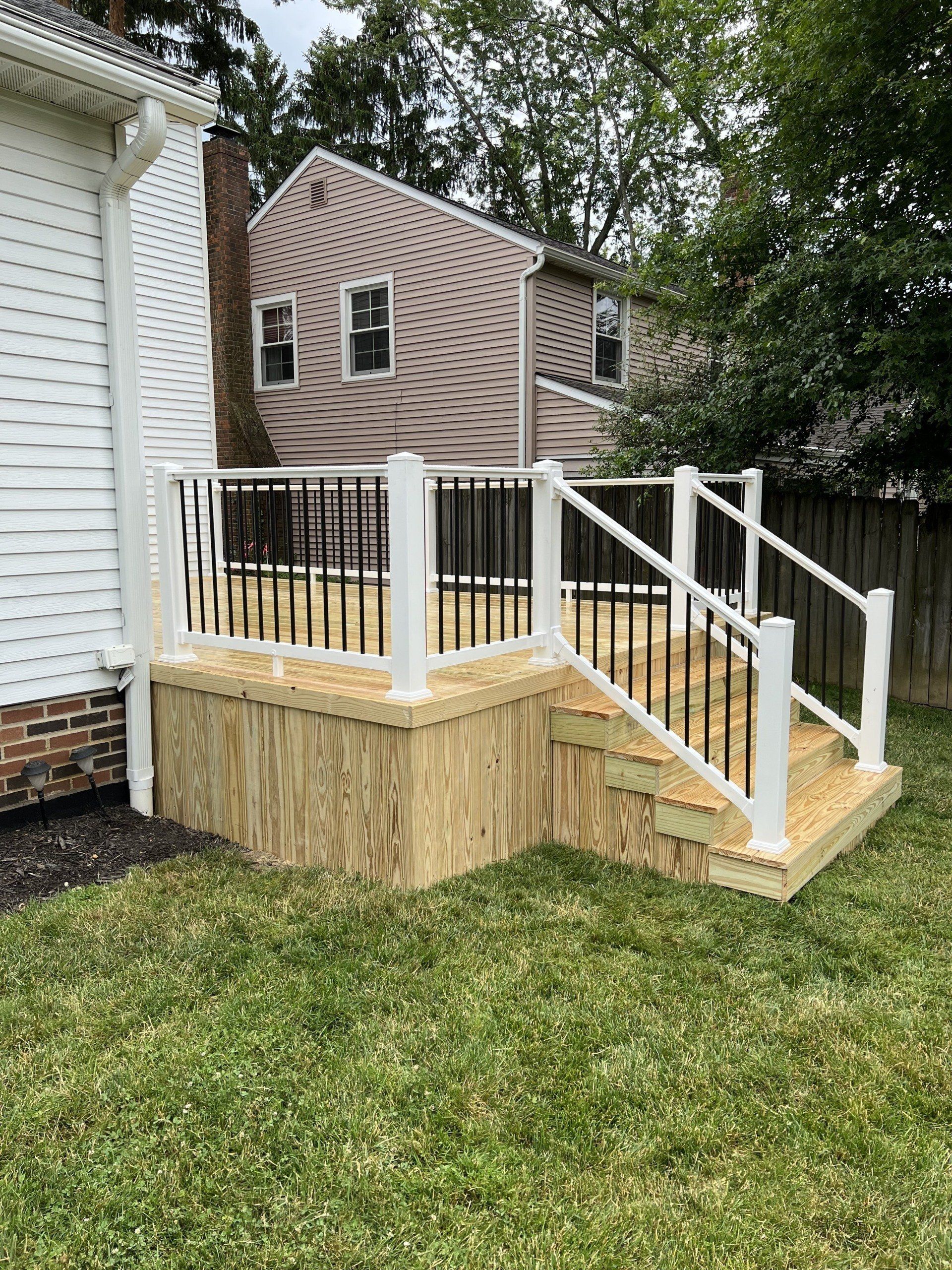 New wooden deck with white railings and black spindles in a backyard.