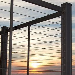Metal railing with horizontal and crisscrossing cables; sunset in background.