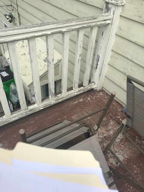 A weathered, painted white balcony railing and floor with peeling paint; an empty chair visible.