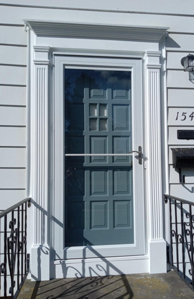 White house entrance with blue-gray door and ornate white trim, visible through a screen door.
