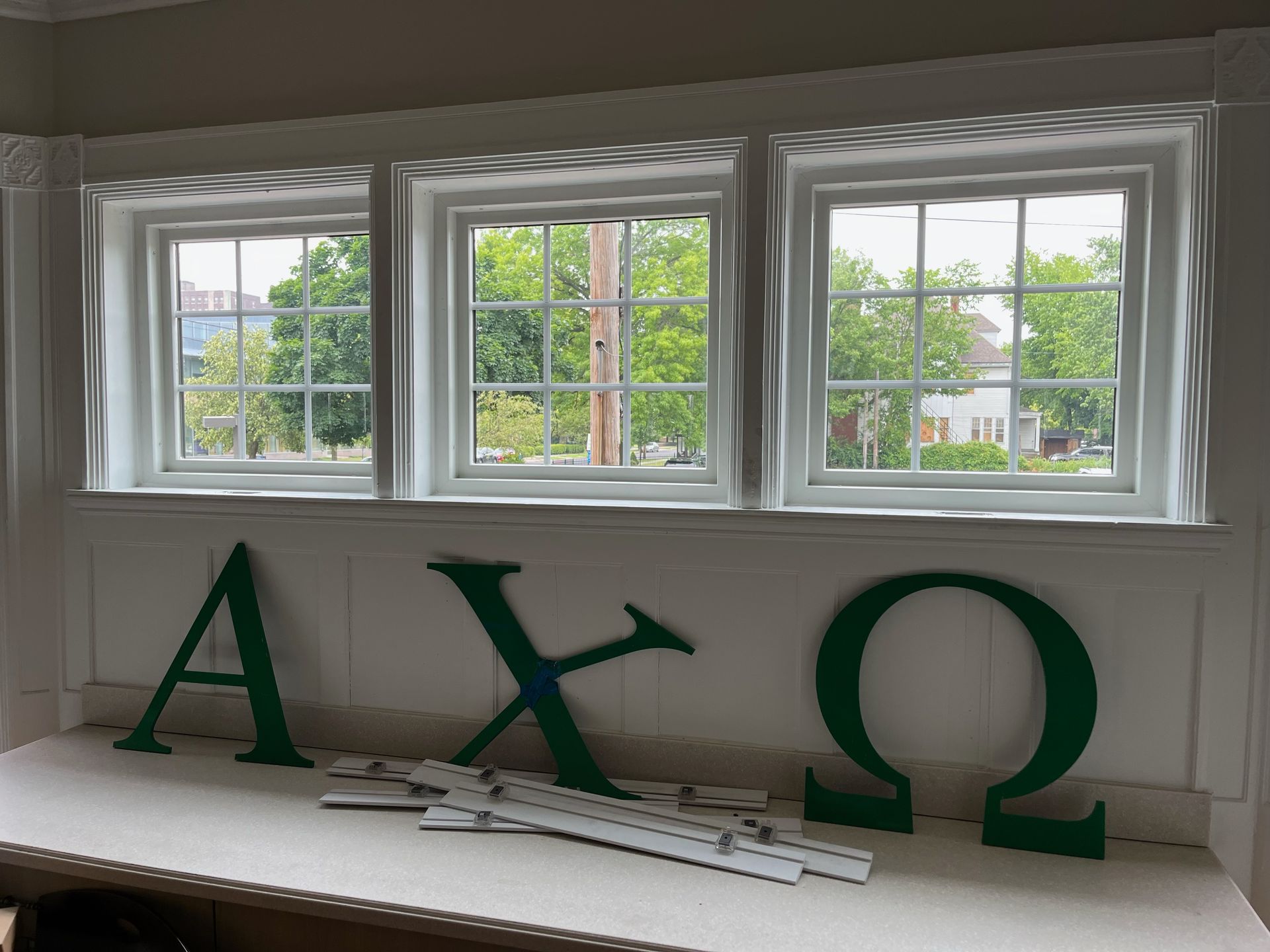Three white-framed windows above a counter, with green Greek letters A, X, and Ω on it.