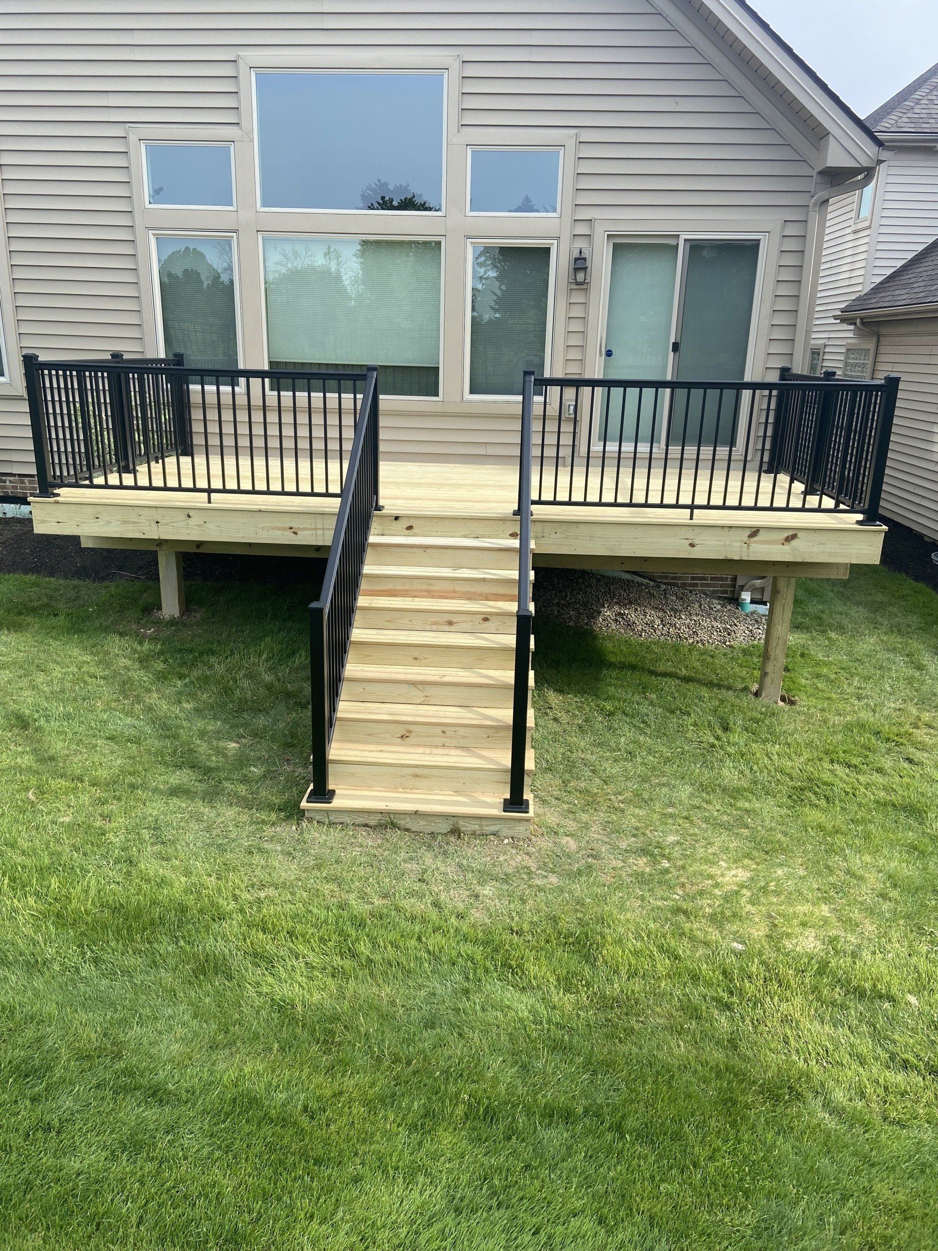 Wooden deck with black railings and steps leading to a house with a large window.