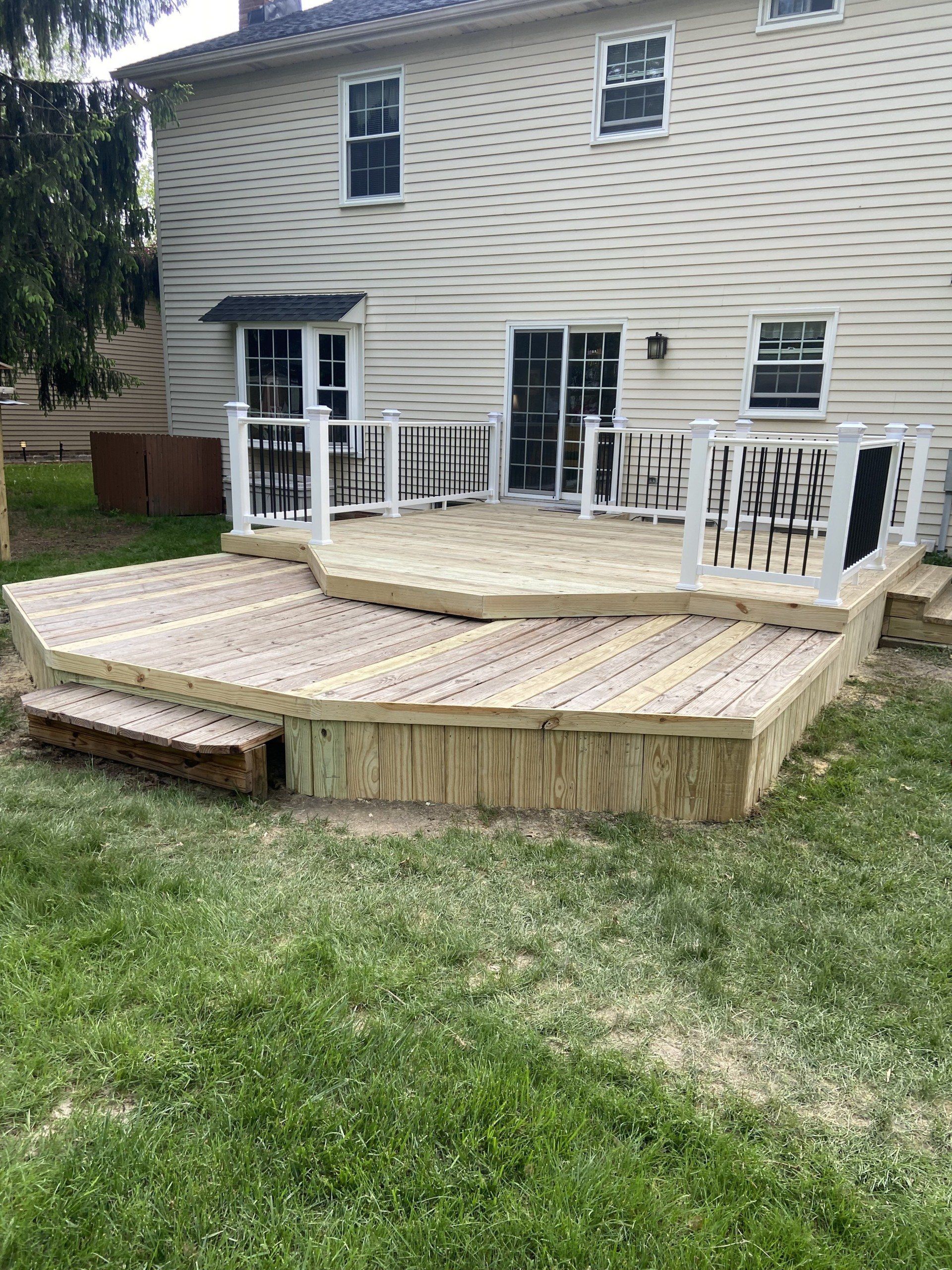 Wooden deck with steps, railings, and backyard view of a house.