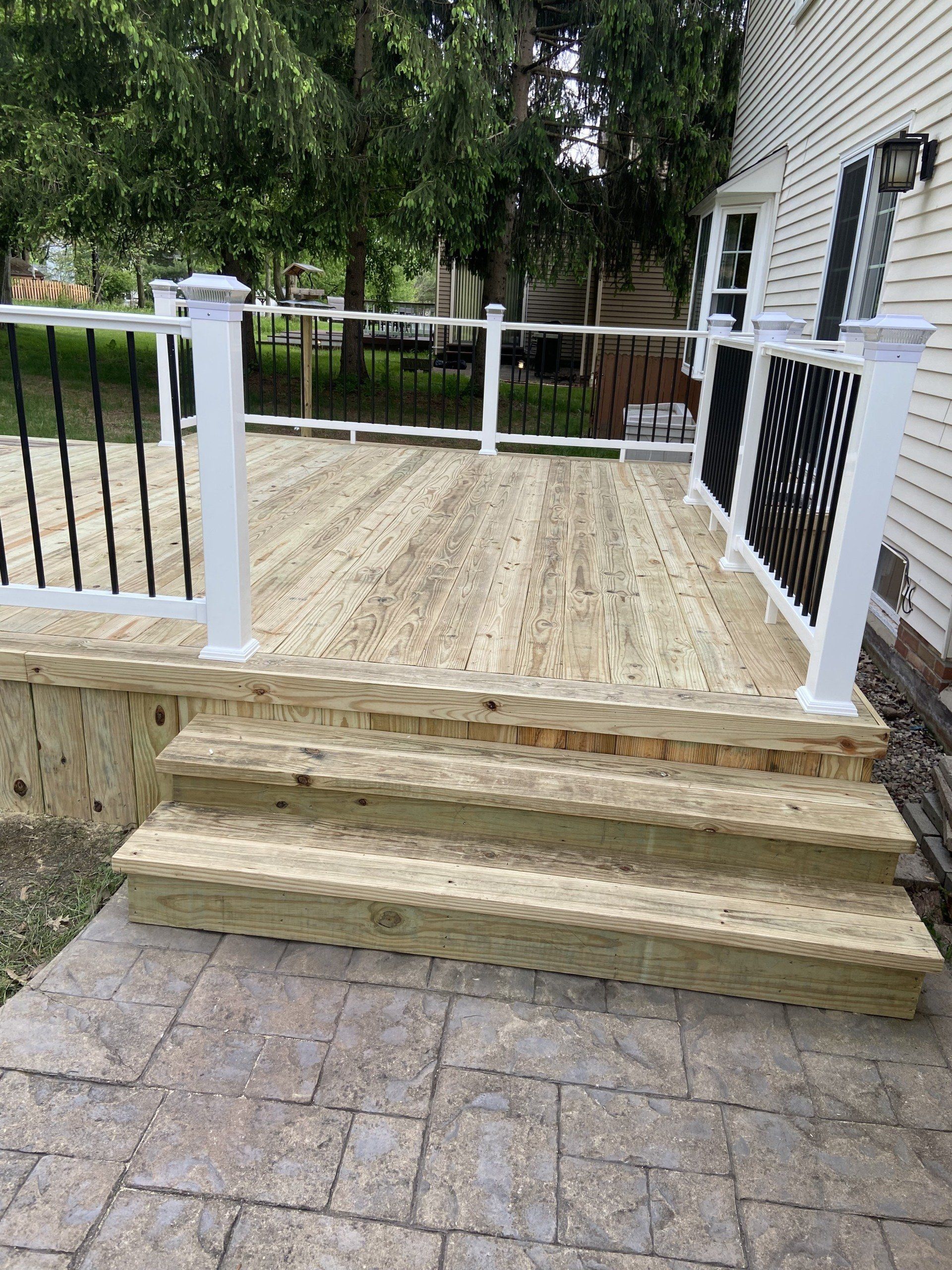 Wooden deck with steps, black railing, and white posts. Patio stones lead to the steps.