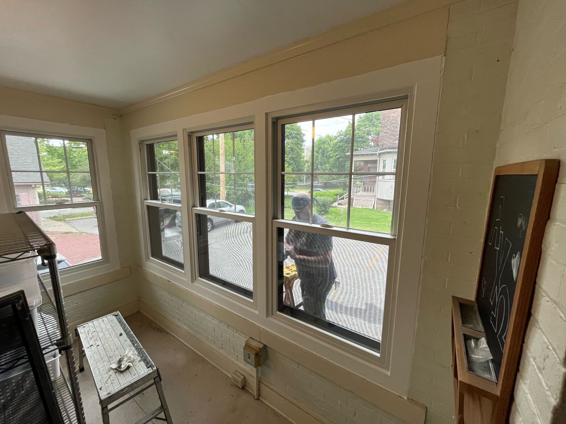 Sunroom interior with three windows, person visible through the middle window, small chalkboard on the right.