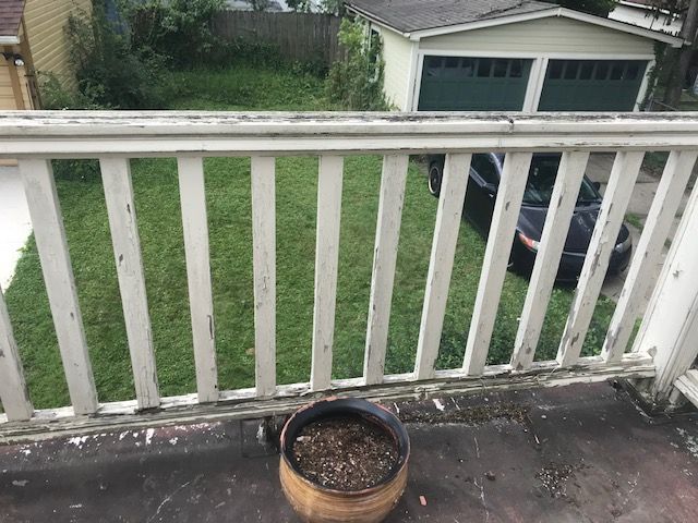 Wooden railing on a porch, view of a yard and garage. A pot sits on the porch.