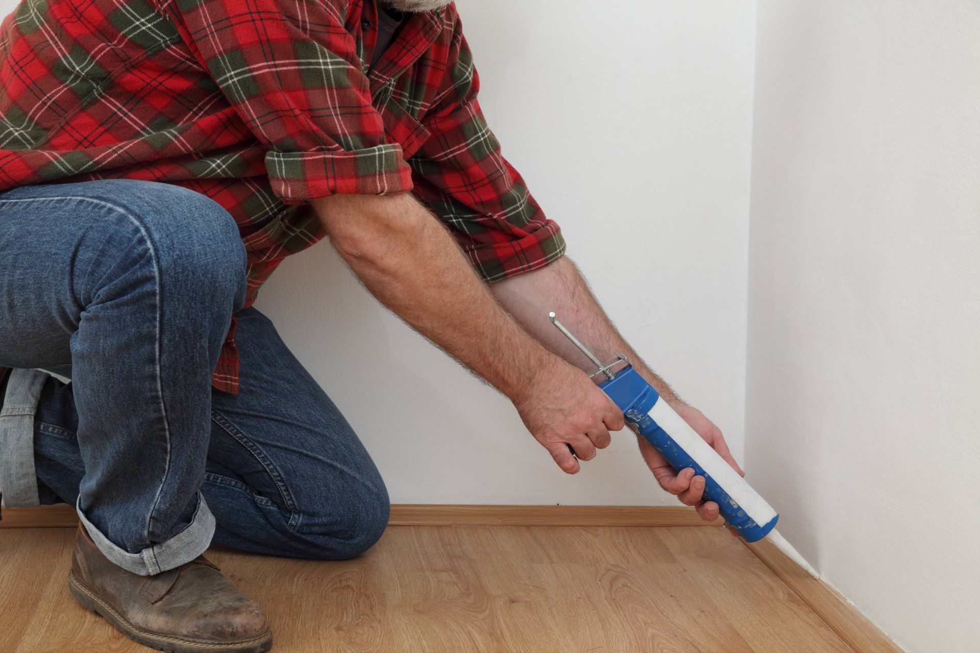 Person applying caulk to a floor molding against a white wall with a caulk gun.