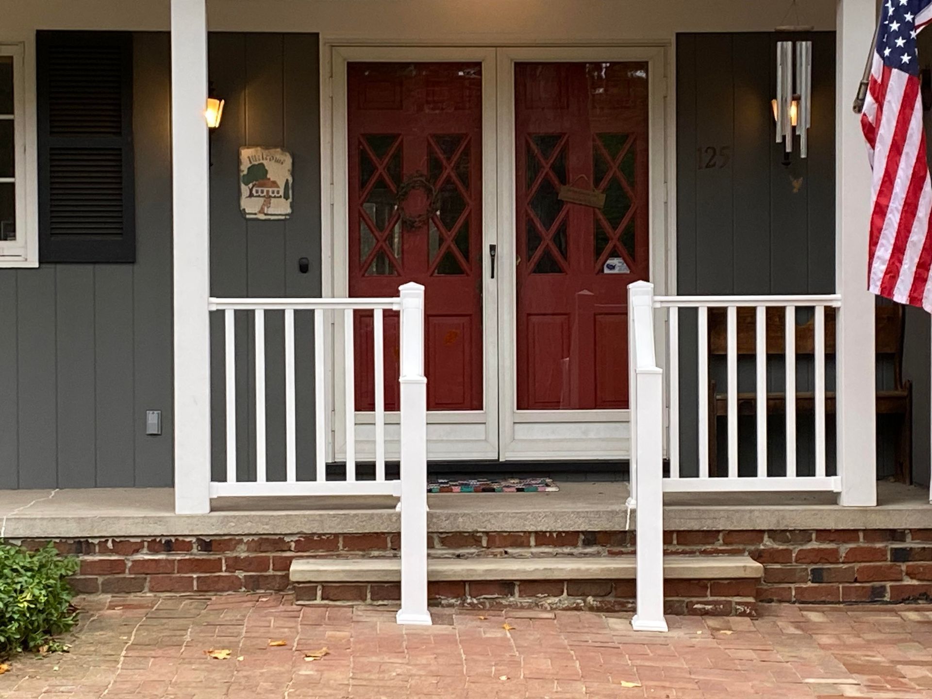 White railing on a porch with red doors, American flag, and gray siding.