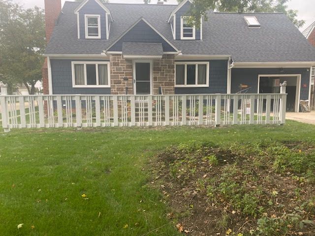 Blue house with white trim, stone facade, and white picket fence on green lawn.