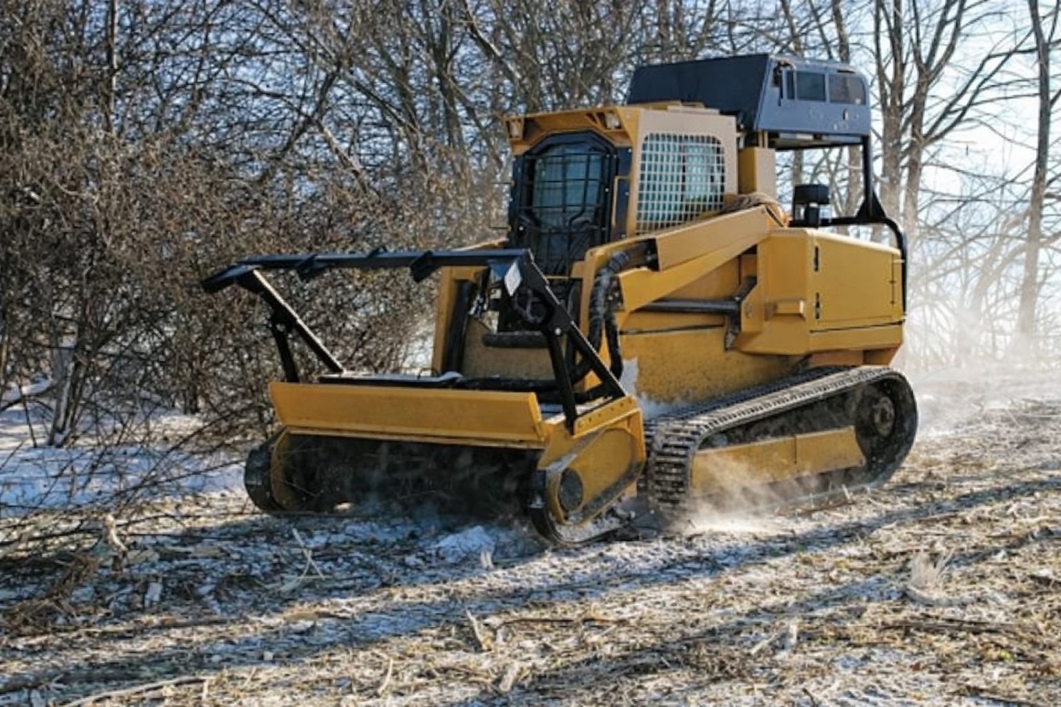Yellow bulldozer clearing brush in a snowy field beside bare trees
