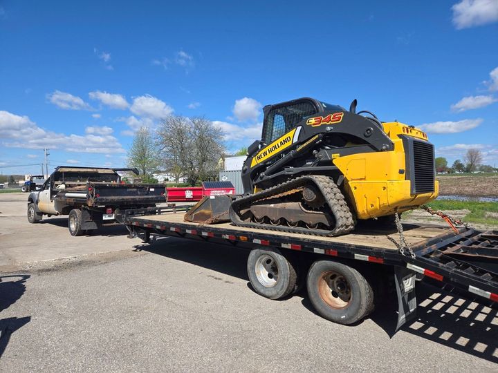 Yellow skid steer on a flatbed trailer parked in a lot under a blue sky