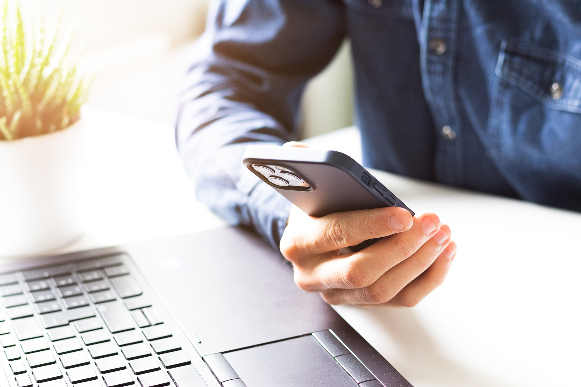 a man is holding a cell phone in front of a laptop .