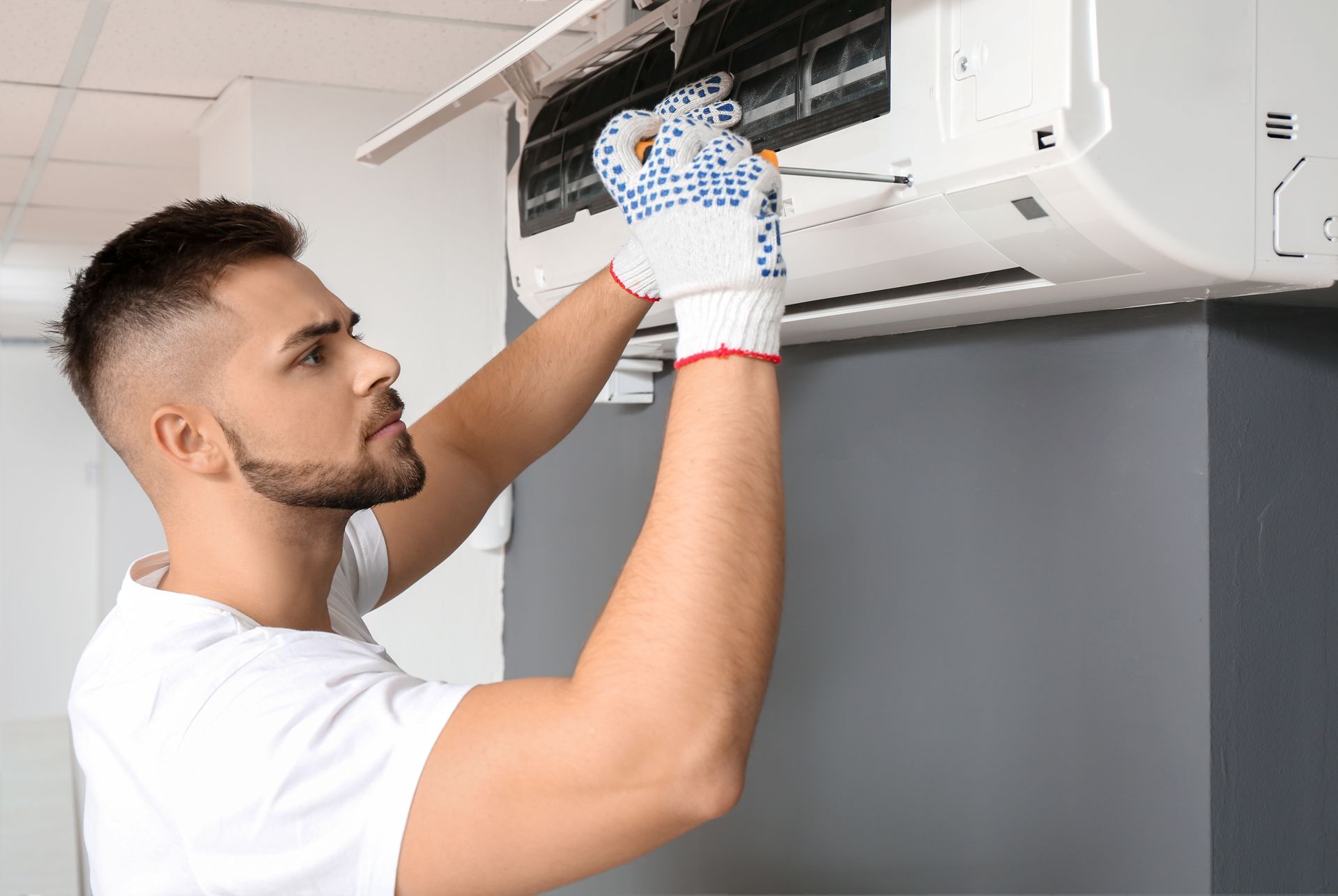 A technician is repairing an air conditioner indoors.