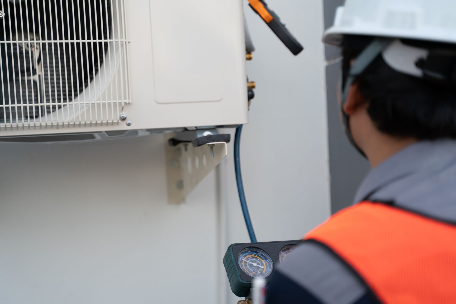 HVAC TECHNICIAN SERVICING OUTDOOR AIR CONDITIONING UNIT WITH GAUGES DURING MAINTENANCE CHECK SERVICE.