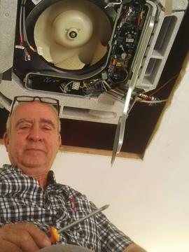 Un uomo che tiene in mano degli attrezzi sotto un'unità di climatizzazione a soffitto aperta, guarda verso la telecamera.