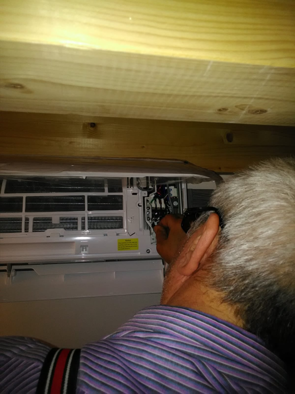 Una persona ispeziona un condizionatore d'aria a parete con cavi a vista sotto un soffitto di legno.