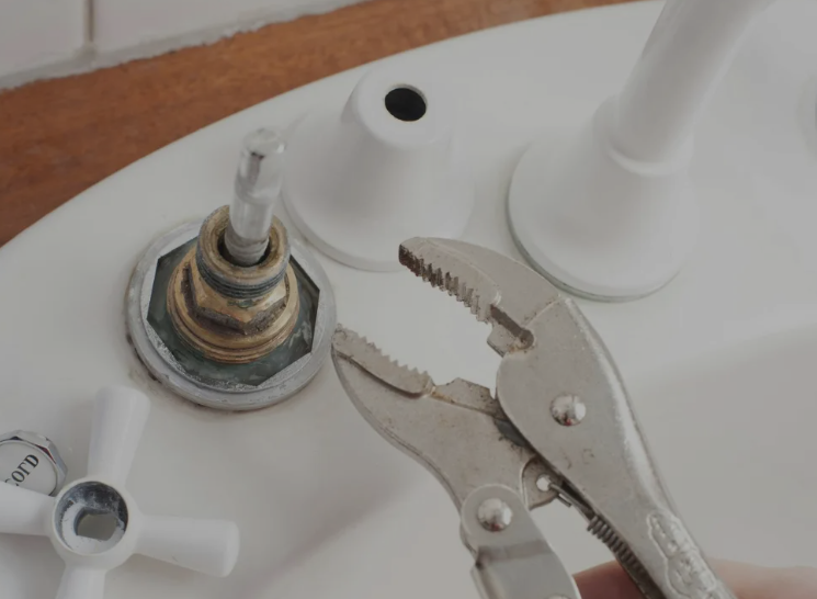Pinze che afferrano una valvola del rubinetto corrosa su un lavandino bianco o sulla cassetta del WC.