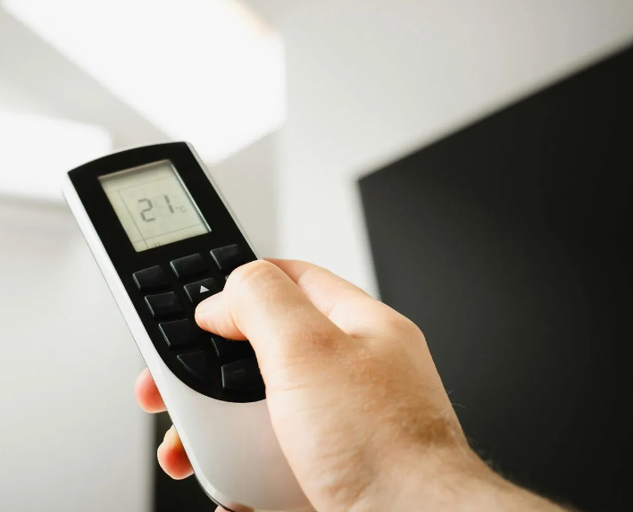 Mano che regola un telecomando puntato verso un'unità a parete che visualizza 21 °C