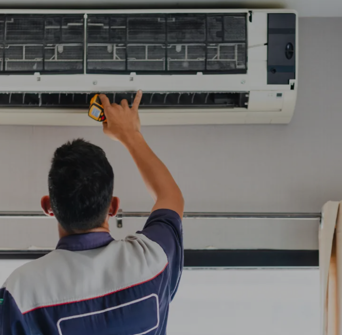 Tecnico che pulisce un condizionatore d'aria a parete con uno spruzzino in un ambiente interno.