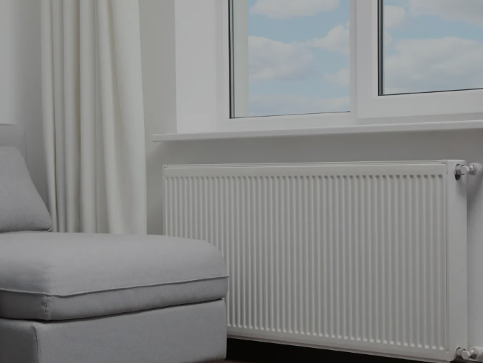 Divano grigio accanto a un termosifone bianco sotto una finestra con tende