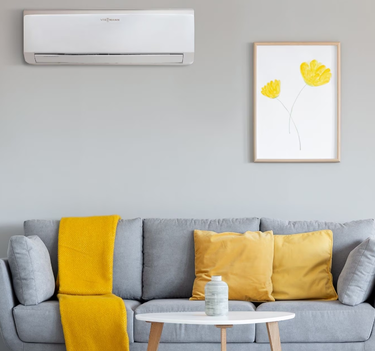 Soggiorno moderno grigio con dettagli gialli, condizionatore a parete, quadri incorniciati e divano con cuscini e coperta.