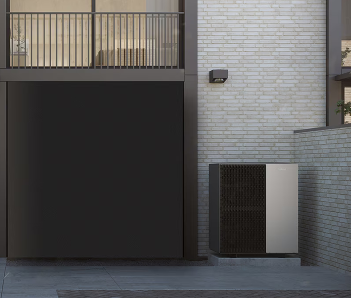 Facciata moderna dell'edificio con balcone, porta del garage scura, muro in mattoni e unità esterna di climatizzazione.
