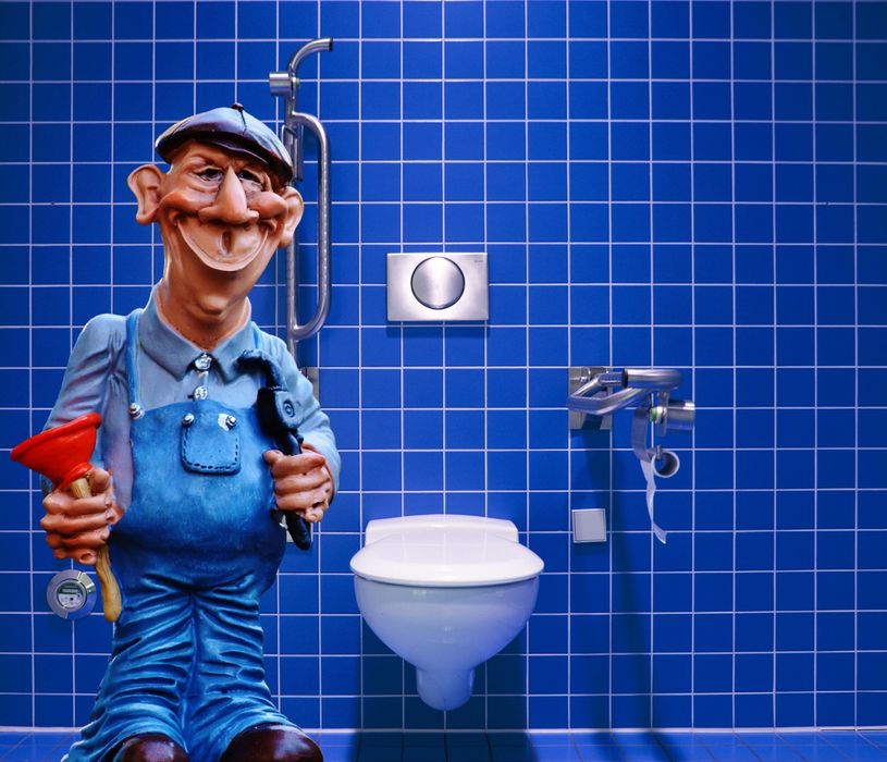 Un idraulico dei cartoni animati che tiene in mano uno sturalavandini rosso in un bagno piastrellato di blu, accanto a un WC e a un lavandino.