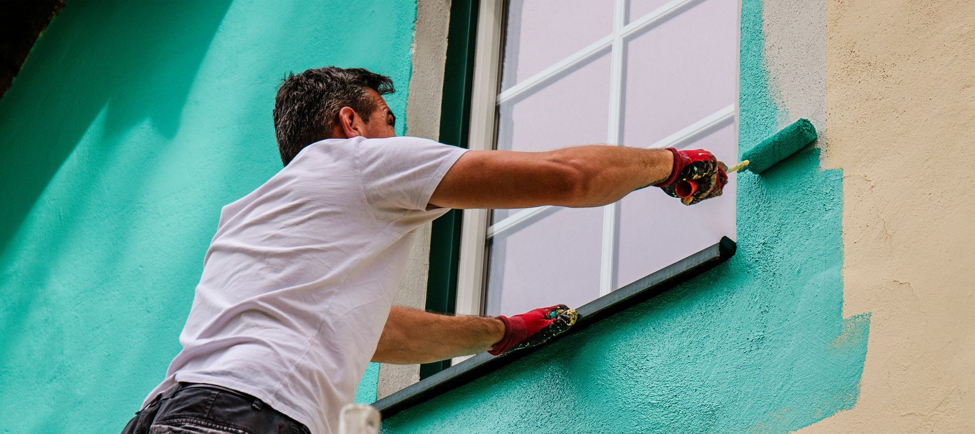Person in a white shirt painting a turquoise wall with a roller from a ladder