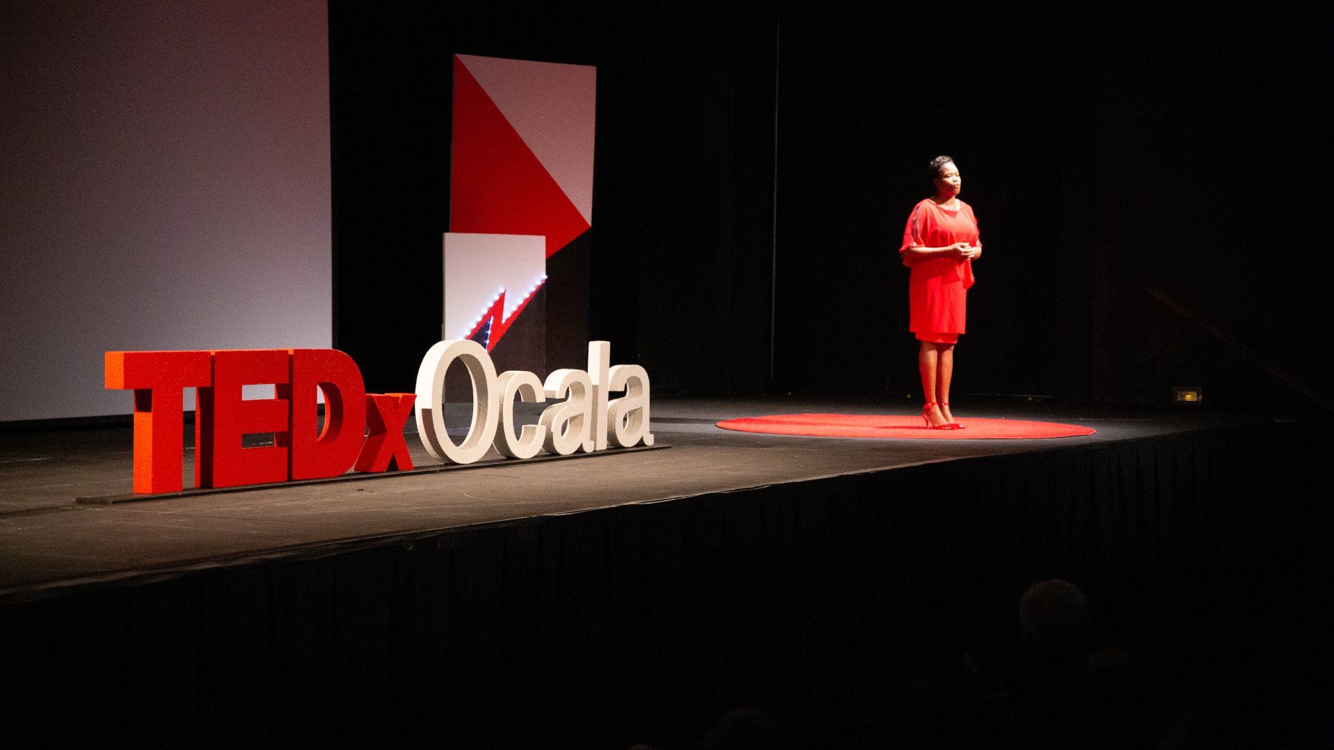A woman in a red dress is standing on a stage in front of a ted ocala sign