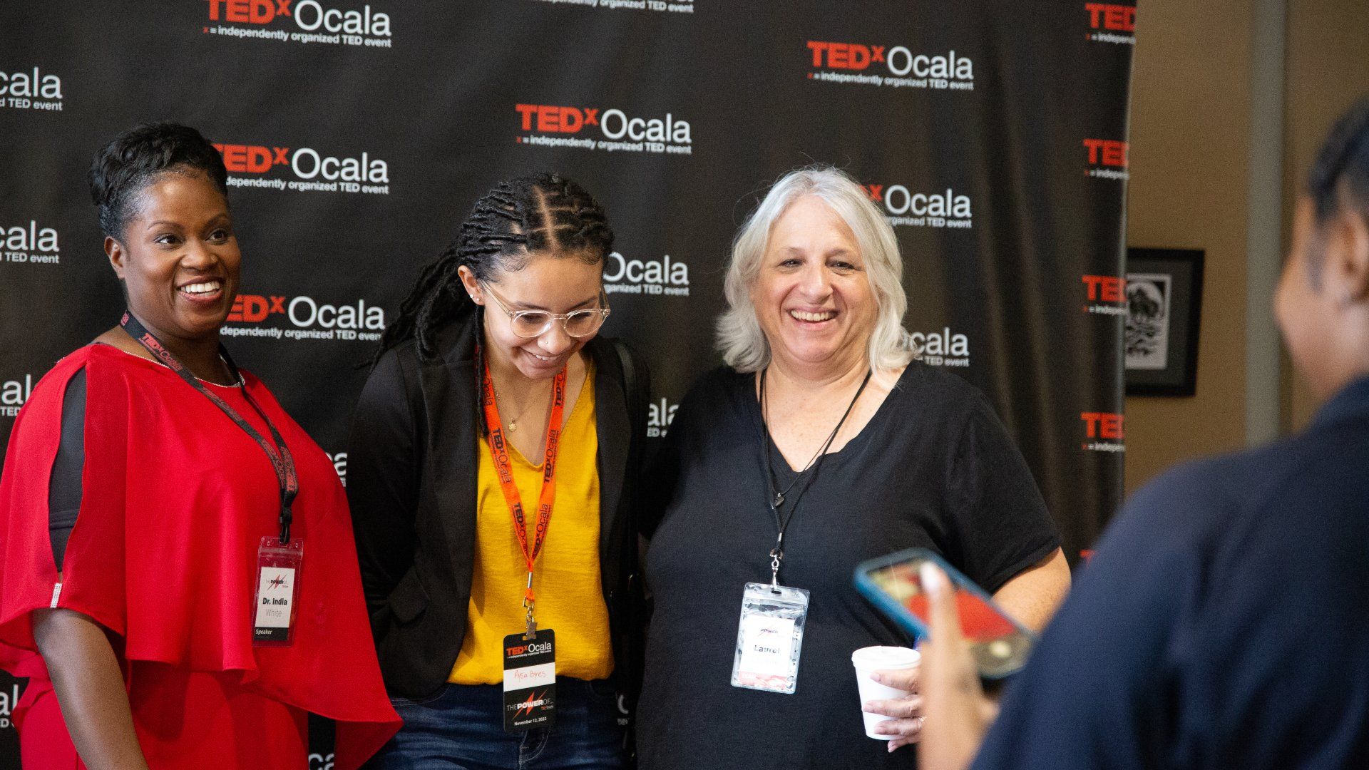 A group of women are posing for a picture in front of a ted talk backdrop.